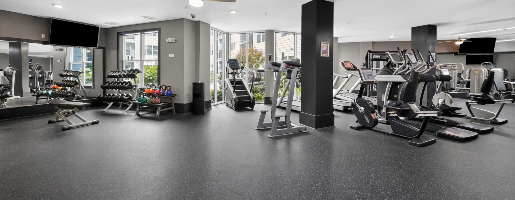 State-of-the-art fitness center at One305 Central apartments in Charlotte, NC with a row of treadmills and ellipticals, a mirrored wall, a free-weight rack, and floor-to-ceiling windows
