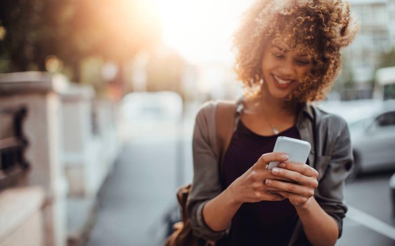 woman texts on her phone as she walks through the city