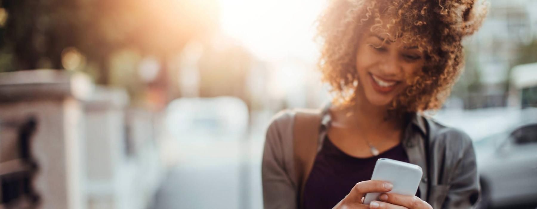 woman texts on her phone as she walks through the city